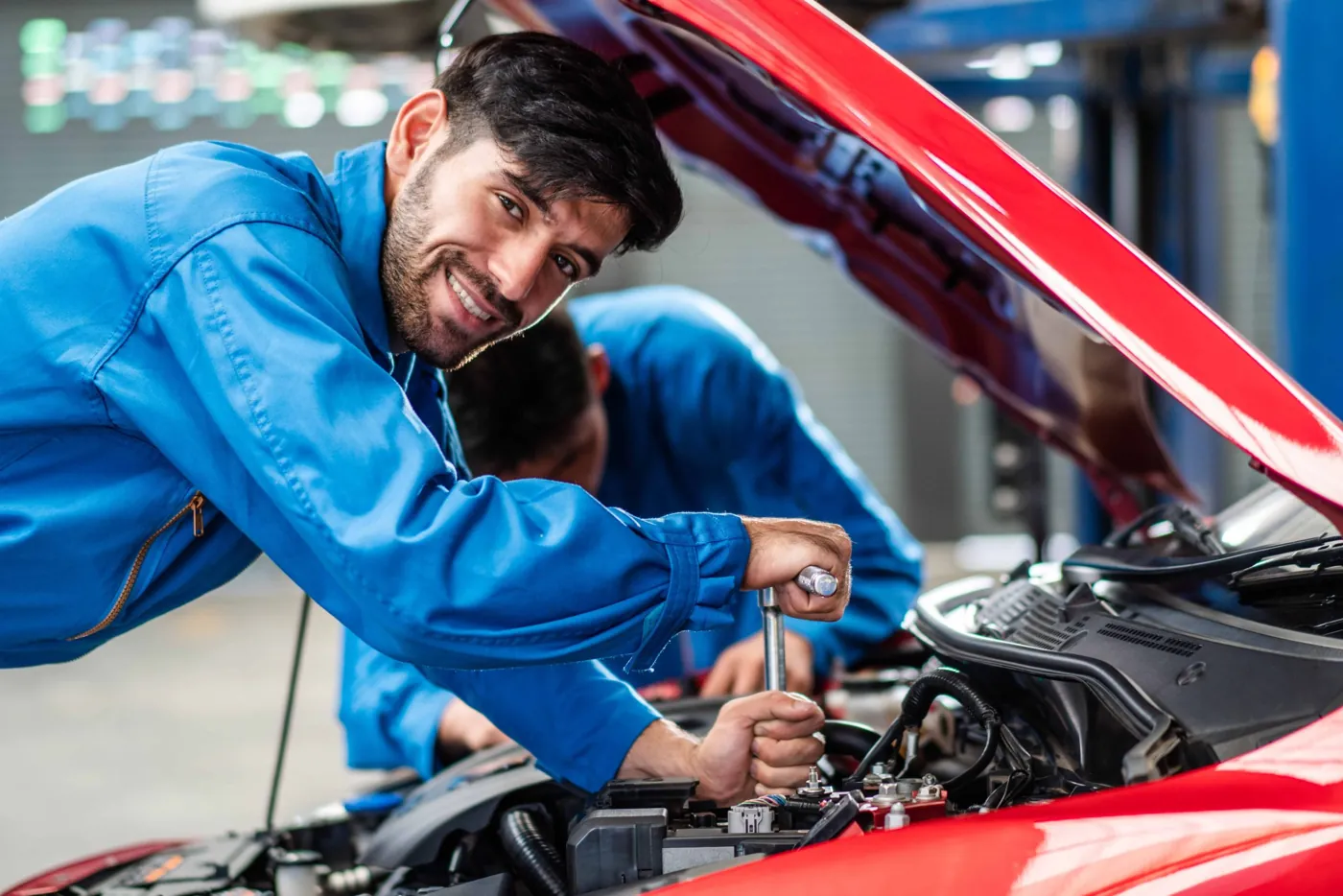 Meccanico sorridente al lavoro sotto il cofano di un'auto